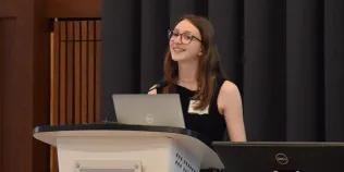 Photo of a student standing at a podium delivering a talk