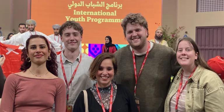 Photo of four students and their tutor at a literary festival. They are smiling at the camera.