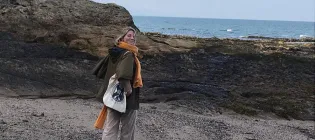 Photo of Elisabeth standing on the seashore looking directly at the camera