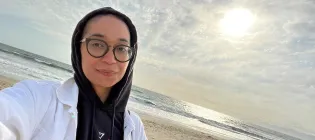 Head and shoulders photo of Francisca Da Silveira on a beach with her hood up