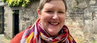 Photo of Lynn standing outside in a cobbled lane looking at the camera