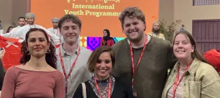 Photo of four students and their tutor at a literary festival. They are smiling at the camera.