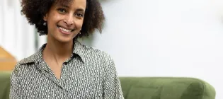 Zebib K Abraham on a green sofa, smiling at the camera with her head titled.