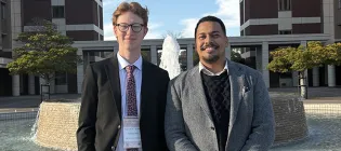 Cameron Bain and his mentor standing in front of a fountain on a university campus in Japan. There are two towers in the background.