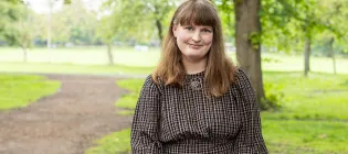 Photo of Suzanne sitting in a parkland setting. She is smiling at the camera.