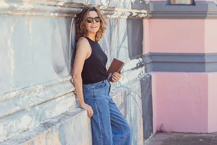 Ines Arteta leaning against a wall and looking at the camera with a book in her hand
