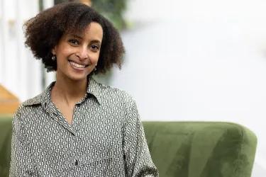 Zebib K Abraham on a green sofa, smiling at the camera with her head titled.