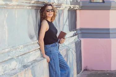 Ines Arteta leaning against a wall and looking at the camera with a book in her hand