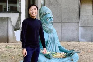 Photo of a student on the left with a statue of Tamil poet Thiruvalluvar 