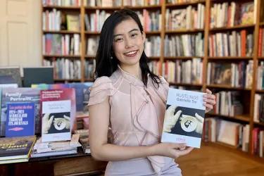Photo of a student sitting on a table in a book shop holding up her poetry pamphlet