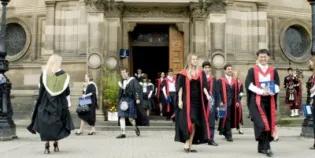 A group of students wearing academic dress walk out of McEwan hall
