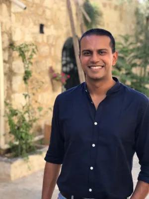 Photo of Dr Shadaab Rahemtulla. There is a wall behind him and various plants and flowers.  