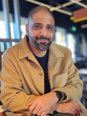 Anjum Naqvi sitting at a table, smiling at the camera.