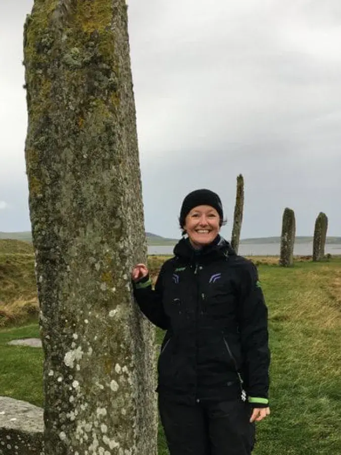 Astrid Nyland at a neolithic site smiling at the camera with her hand on one of the standing stones