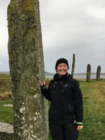Astrid Nyland at a neolithic site smiling at the camera with her hand on one of the standing stones