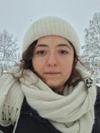 a photo of Erika di Vivo, backdropped with a snowy background and wearing a hat and scarf