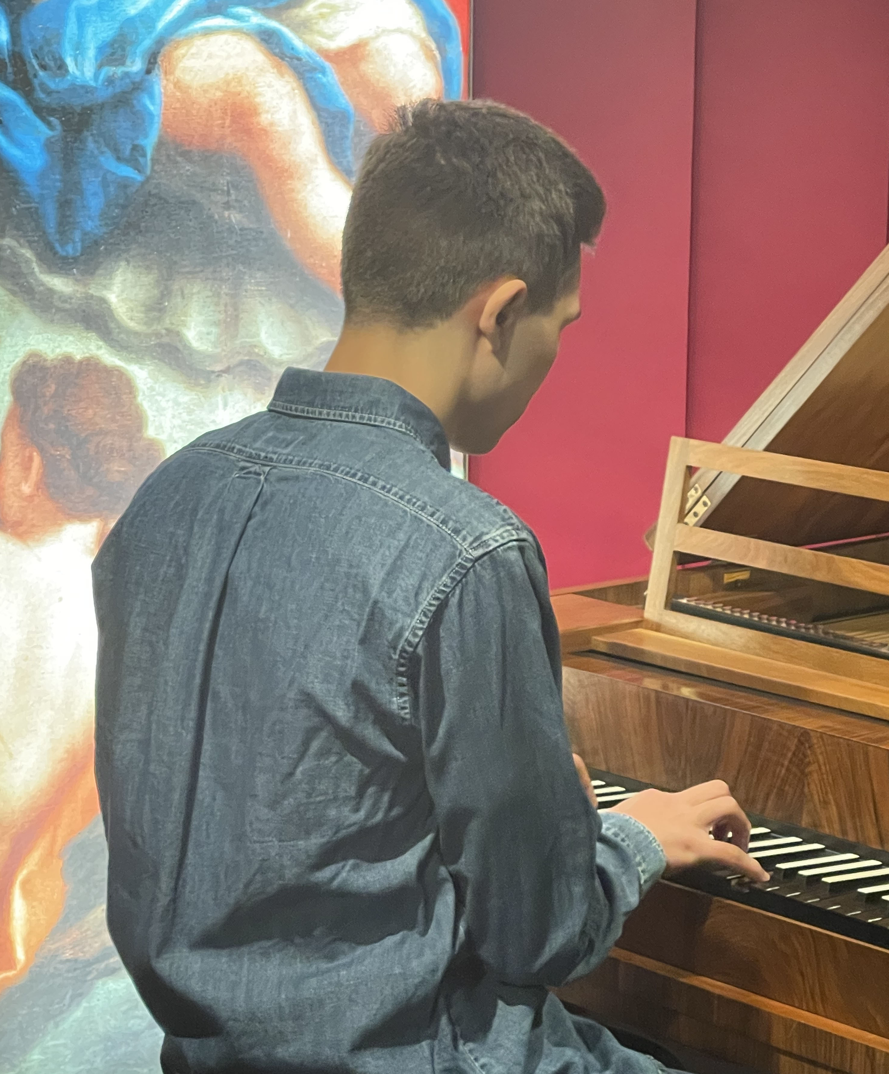 Photo of a young man playing a reproduction piano at St Cecilia's Hall. He is seen seated, from the back.