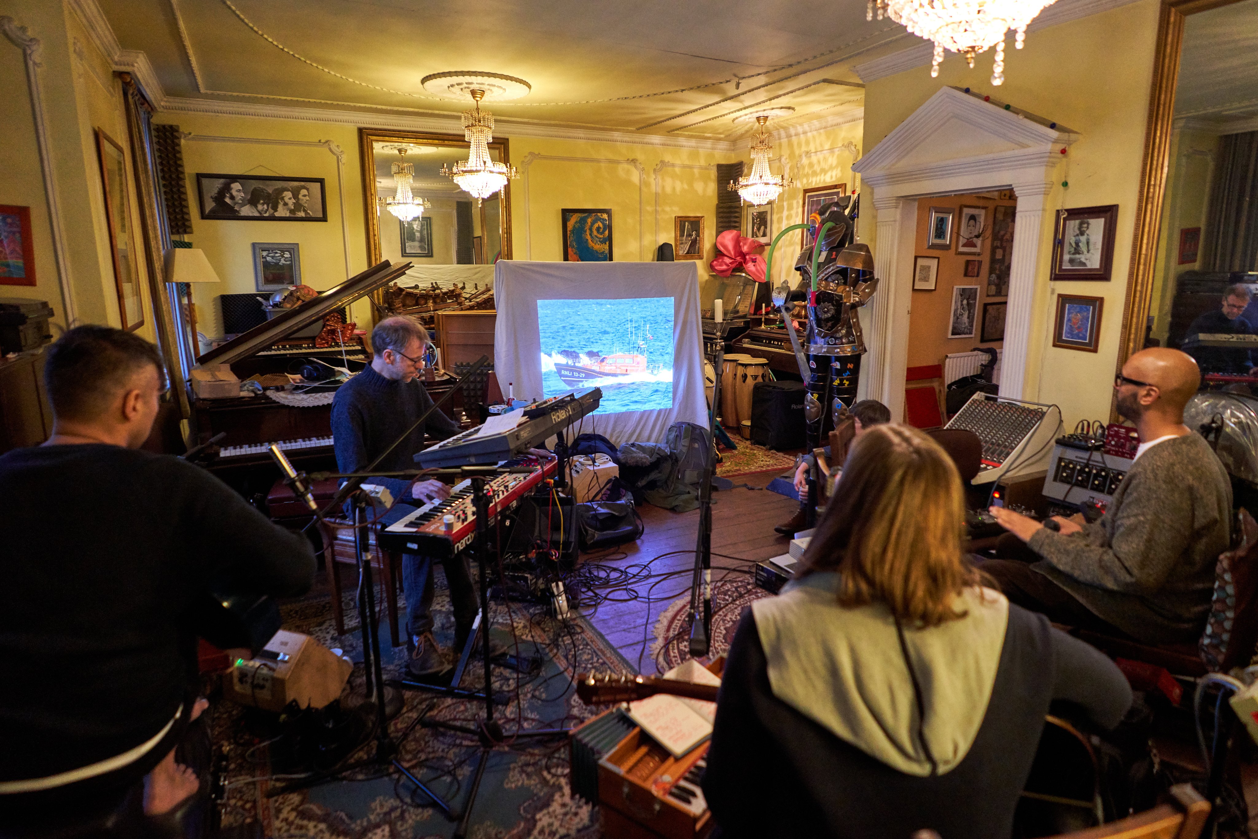 Photo of performers playing music in front of a screen showing archival footage