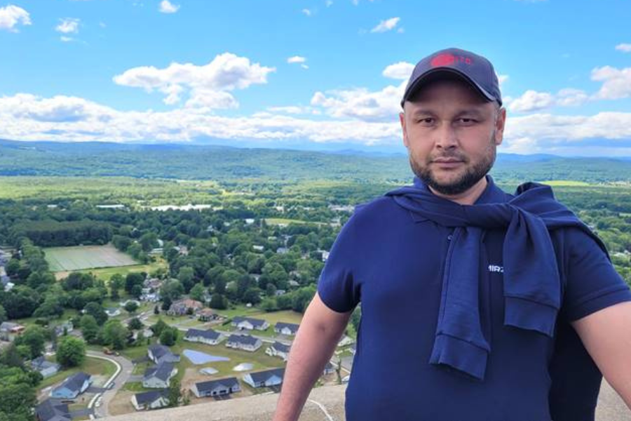 Iskandar Sattibaev smiling at the camera with green hills and forrest in the background