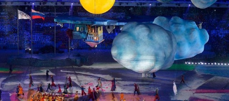 a shot of the opening ceremony of the Olympics in a big stadium; you can see flags, fake clouds and performers