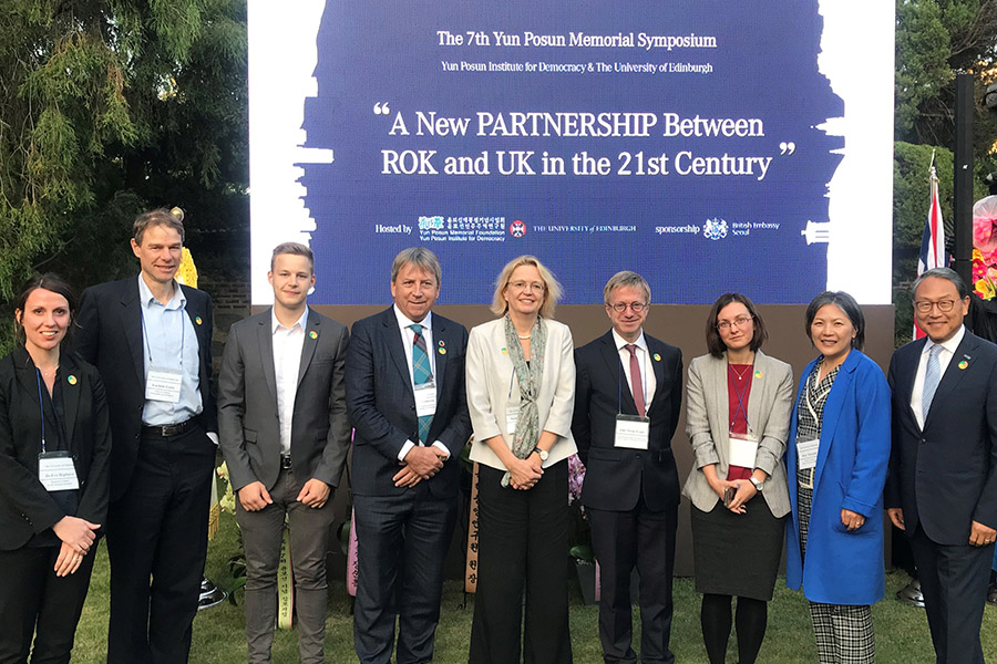 Nine conference delegates standing in front of a conference banner